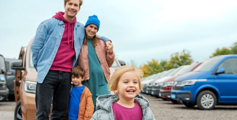 Eine strahlende Familie erkundet das Angebot von Volkswagen auf einem Gebrauchtwagenmarkt