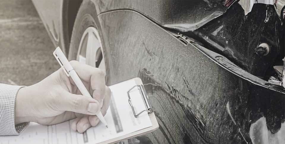 Eine Hand hält einen Stift und notiert die Schäden an einem Unfallwagen während der Rückgabe des Leasingfahrzeugs